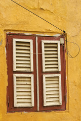 An old wooden window with closed shutters in a yellow ochre painted brick wall in Willemstad,...