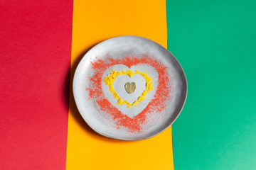 Heart made of ground red pepper,  turmeric, bay leaf on gray plate on red, green and yellow background as symbol of traffic light