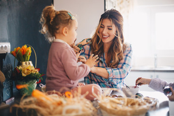 A mother with her two daughters having fun while painting eggs for Easter.