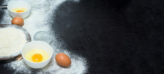 Ingredients for baking. Bowl, eggs, flour, egg beater, on a black Board on top. baking background, top view, place to copy text, measure, recipe. Banner