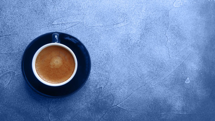 Cup of freshly brewed espresso on a saucer on a textured classic blue background