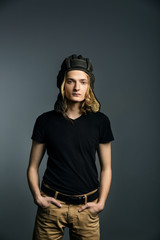 Young guy model posing in a tankman helmet on the gray background. hands in pockets