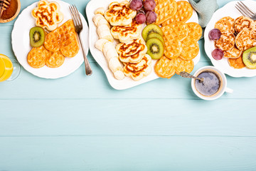 Healthy breakfast with fresh hot waffles hearts, pancakes flowers with berry jam and fruits on turquoise background, top view, flat lay. Food concept. Copy space.