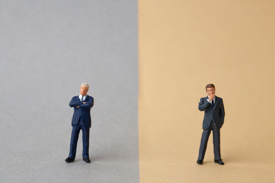 miniature two businessmen stand on opposite sides 