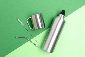 Metal bottle, drinking tube and cleaning brush. Zero waste accessories on green background.