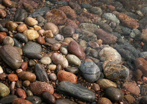 Bunte, runde, abgeschliffene Steine liegen am Strand in der Sonne und werden vom Wasser umsp&uuml;lt