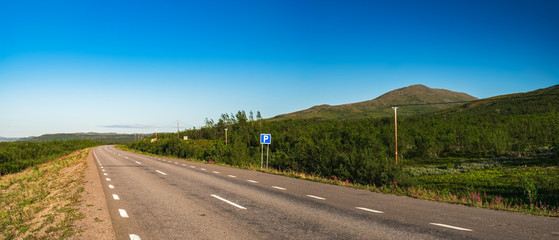 Summer landscape with green grass, asphalt road and mountains on horizon in Lapland, near the norwegian border in Sweden. Swedish landscape in summertime.