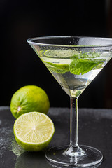 Close-up of cocktail glass with mint leaves and lime slice, on black background with a lime and a half with selective focus on vertical