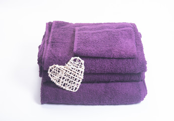 Stack of purple towels with wicker heart on white background 