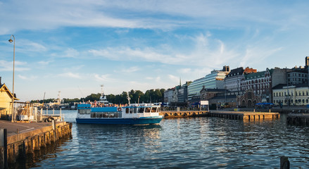 Tourist ship in Old Port of Helsinki, Finland, boat with tourists arrives ashore. Scenic summer panorama of Port pier architecture in Old Town under blue cloudy sky