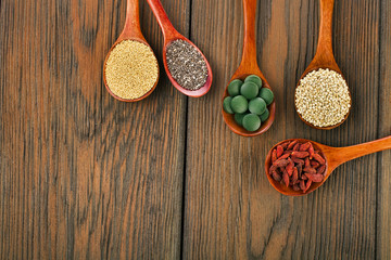 Goji berries, amaranth seeds, chia seeds, quinoa seeds, spirulina tablets in the spoons on a wooden background.