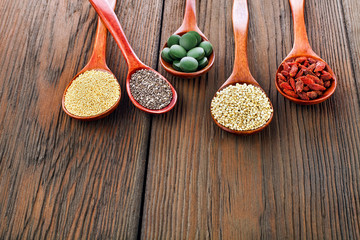 Goji berries, amaranth seeds, chia seeds, quinoa seeds, spirulina tablets in the spoons on a wooden background.
