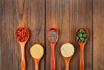 Goji berries, amaranth seeds, chia seeds, quinoa seeds, spirulina tablets in the spoons on a wooden background.