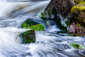 Mossy stones in a stream of water. Long exposure.