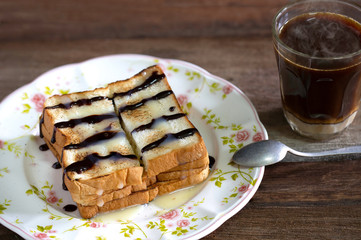 Toasted toast pour with sweetened condensed milk and chocolate in white dish flower patterned and black coffee in glass