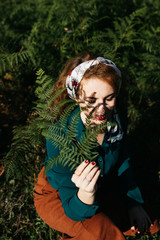 Portrait of beautiful woman with curly hair holding fern. Shadows of fern are on her face. 