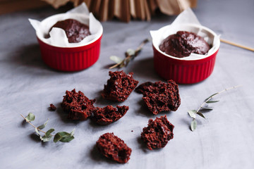 Chocolate muffins in red cups. Small glazed ceramic ramekin with brown cakes on a gray and white background.