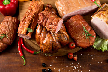 Composition of different smoked meat with spices and herbs on wooden background