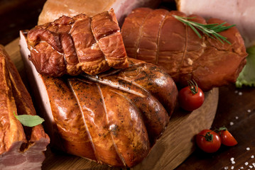 Composition of different smoked meat with spices and herbs on wooden background