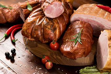 Composition of different smoked meat with spices and herbs on wooden background
