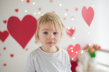 Obraz na płótnie Canvas Cute blonde toddler boy, holding box in heart shape and flowers