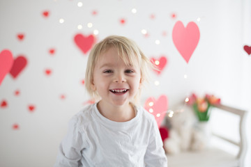 Fototapeta na wymiar Cute blonde toddler boy, holding box in heart shape and flowers