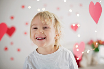 Obraz na płótnie Canvas Cute blonde toddler boy, holding box in heart shape and flowers