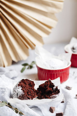 Chocolate muffins in red cups. Small glazed ceramic ramekin with brown cakes on a gray and white background.