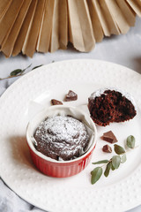 Chocolate muffins in red cups. Small glazed ceramic ramekin with brown cakes on a gray and white background.