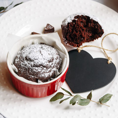 Chocolate muffin in red cup. Mockup valentine black heart copyspace. Small glazed ceramic ramekin with brown cake on a white background.