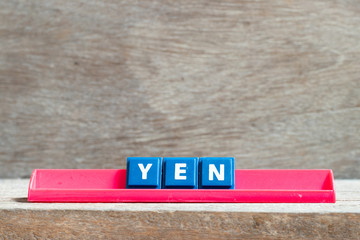 Tile letter on red rack in word yen on wood background