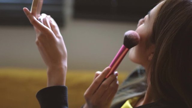 Scene from left side of young Asian woman doing brush on her cheek, shot from opposite the light.