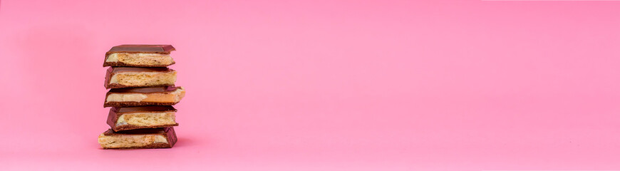 Mountain, a tower of pieces of sweet milk chocolate with a layer of cookies is on a pink background. Holiday concept - valentines day, mothers day. Place for text. Banner. Minimalism. Romance for two.