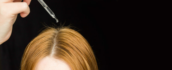 A glass pipette with a hair growth agent is applied to the parting of the hair, red hair. Hair care.