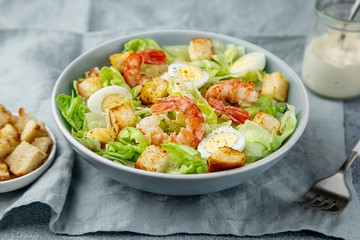 Caesar salad with prawn, roasted chicken,  croutons and cheese in blue bowl