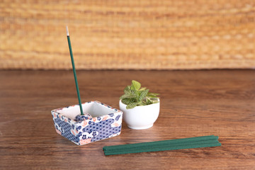Composition with  incense sticks lay on wooden table and one stick is burning in traditional ornamental stand, fresh green plant in pot. Fragrant incense sticks set. Yoga, meditation equipment.