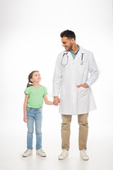 Full length of kid and pediatrician smiling at each other and holding hands on white background