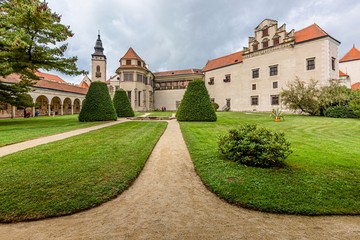 Fototapeta na wymiar Telc / Czech Republic - September 27 2019: View of a state owned castle and a church of James the Great from a garden with green grass, bushes and sandy footpath.