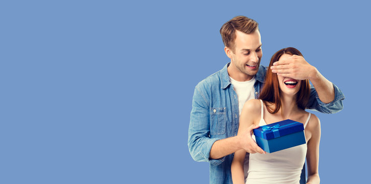 Love, dating, celebrating, lovers concept - happy amorous couple with blue gift box. Blue color background. Copy space for some text.