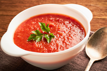 Closeup of tomato soup in a white bowl with a spoon on a wooden table.