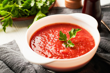 Tomato soup in a white bowl with parsley on a white wooden background