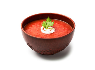 Tomato soup with parsley and milk cream in a brown bowl isolated on white background