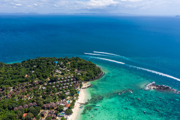Fototapeta na wymiar Blue clear water with boats. Green tropical island Phi Phi, palm trees grow. Shooting from a drone from the air. Beautiful seascape. Turquoise color of the water, you can see the bottom and corals.