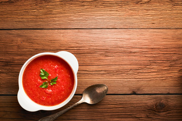 Tomato soup in a white bowl with parsley top view with copy space on a brown wooden background