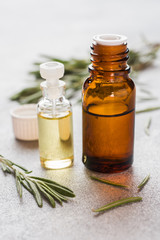 Rosemary essential oil in a glass bottle with fresh branch rosemary herb on grey table for spa,aromatherapy and bodycare.Copy space.