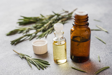 Fototapeta na wymiar Rosemary essential oil in a glass bottle with fresh branch rosemary herb on grey table for spa,aromatherapy and bodycare.Copy space.