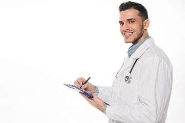 Side view of smiling doctor with clipboard looking at camera isolated on white