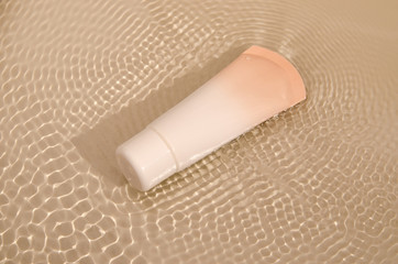 beige tube with makeup foundation cream on water background with little waves