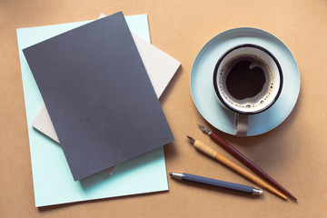 Top view of the workspace. Mock up of three books. Pens, a camera and a cup of coffee on the table.