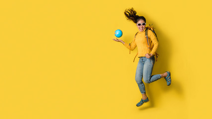 Woman traveler with suitcase, holding ball globe in the hand on Yellow background. Portrait of smiling happy girl with space copy the text. Travel backpack